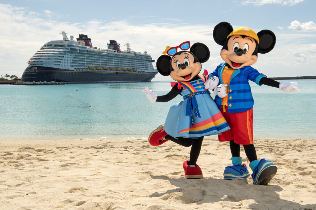 a couple of mickey mouse and minnie mouse on a beach with a cruise ship in the background